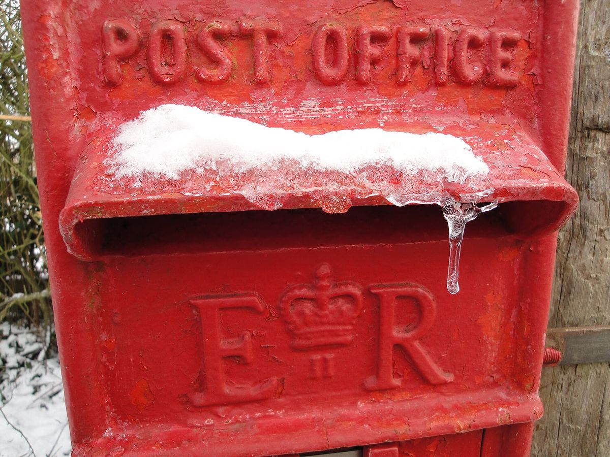 A red Royal Mail post box topped with snow and icicles
